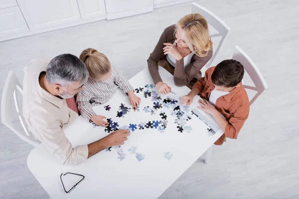 Vue aérienne des enfants avec des grands-parents jouant jeu de puzzle sur la table de cuisine — Photo de stock