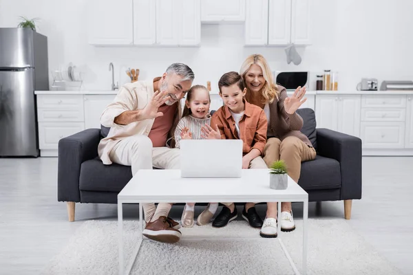 Cheerful kids with grandparents waving hands during video call on laptop — Stock Photo