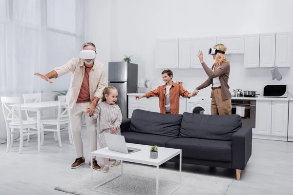 Cheerful kids holding hands with grandparents gaming in vr headsets — Stock Photo