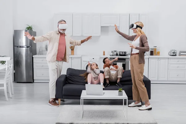 Kids pointing with fingers at grandparents gaming in vr headsets in kitchen — Stock Photo