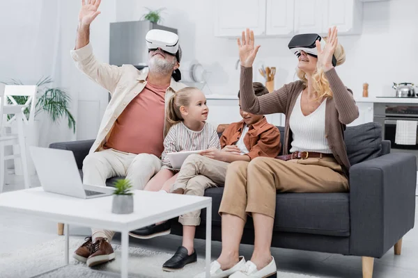 Cheerful couple gesturing in vr headsets near grandchildren with digital tablet — Stock Photo