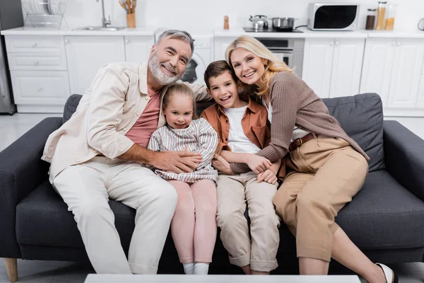 Fröhliches Paar umarmt die Enkel und schaut zu Hause auf dem Sofa in die Kamera — Stockfoto