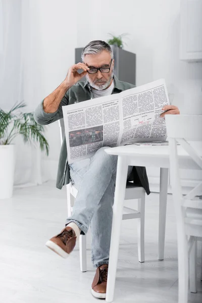 Visão de comprimento total de homem de cabelos grisalhos lendo jornal na cozinha — Fotografia de Stock