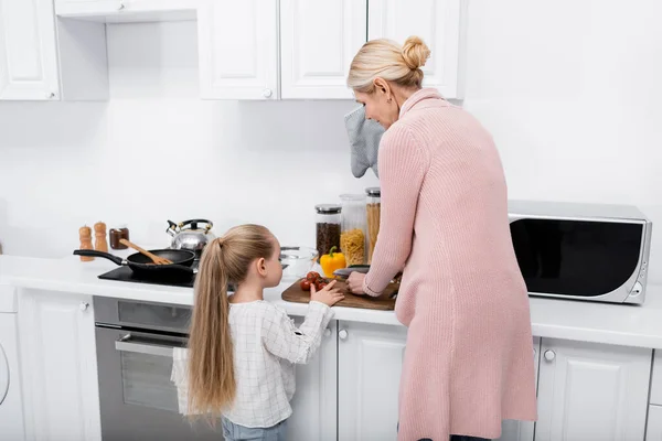 Middle aged woman cutting vegetables near granddaughter in kitchen — Stock Photo