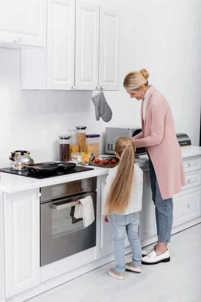 Glückliche Frau mittleren Alters kocht mit Hilfe ihrer kleinen Enkelin in der Küche — Stockfoto