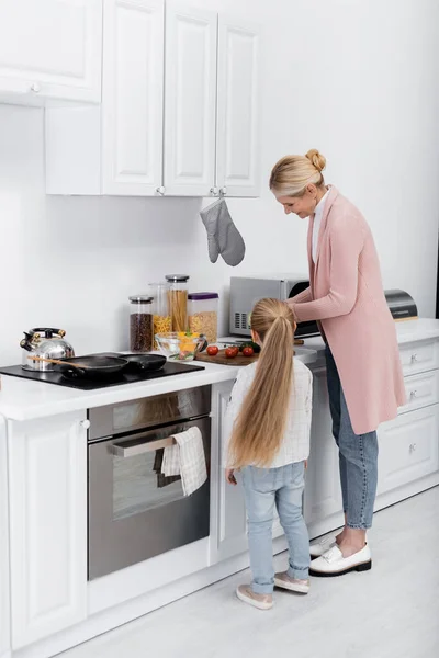 Feliz mujer de mediana edad cocinando en la cocina con la ayuda de la nieta - foto de stock