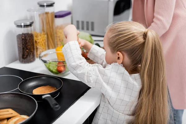 Little girl preparing fresh vegetable salad with granny in kitchen — Stock Photo