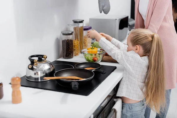 Reife Frau mit kleiner Enkelin bereitet in Küche Salat zu — Stockfoto