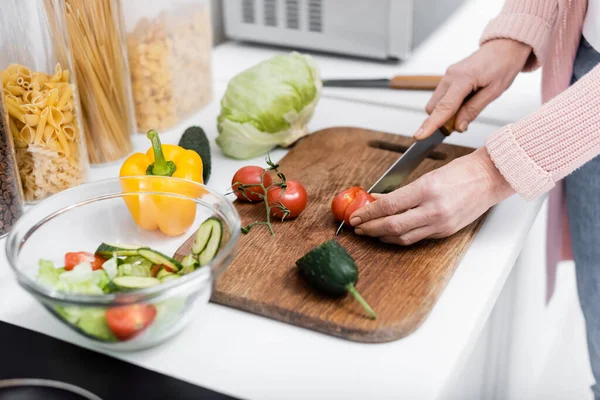 Vista ritagliata della donna che taglia pomodoro ciliegia durante la preparazione di insalata di verdure fresche — Foto stock