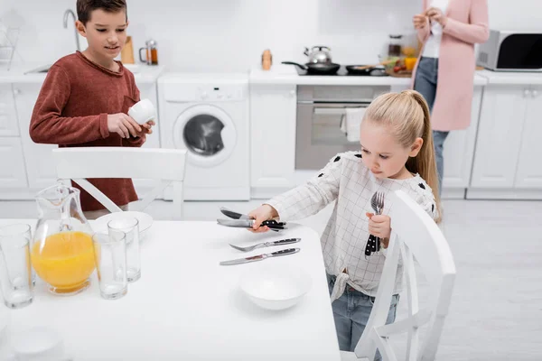 Children setting table in kitchen while granny preparing breakfast — Stock Photo