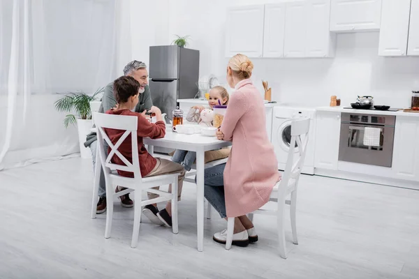 Homem feliz tomando café da manhã com netos e esposa na cozinha moderna — Fotografia de Stock