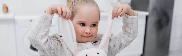 Little girl playing with toy bunny in kitchen, banner — Stock Photo