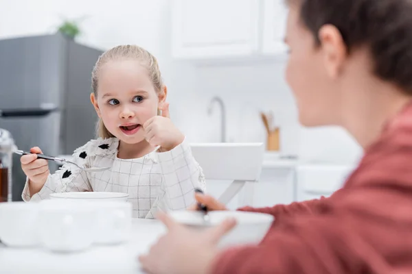 Girl having breakfast in kitchen together with blurred brother — Stock Photo