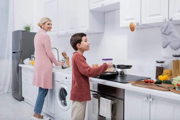 Хлопчик готує млинець біля свіжих овочів і усміхається бабуся на кухні — стокове фото
