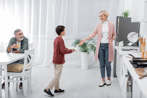 Senior trinkt Orangensaft, während Enkel Oma in Küche hilft — Stockfoto