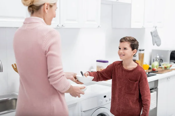 Lächelnder Junge schenkt Großmutter Schüssel, während er ihr in der Küche hilft — Stockfoto