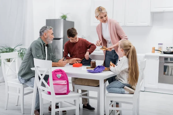 Mujer de mediana edad hablando con su nieta mientras prepara sándwiches en la cocina - foto de stock