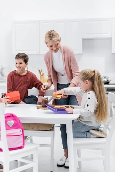 Happy middle aged woman preparing sandwiches with chocolate paste for grandchildren — Stock Photo