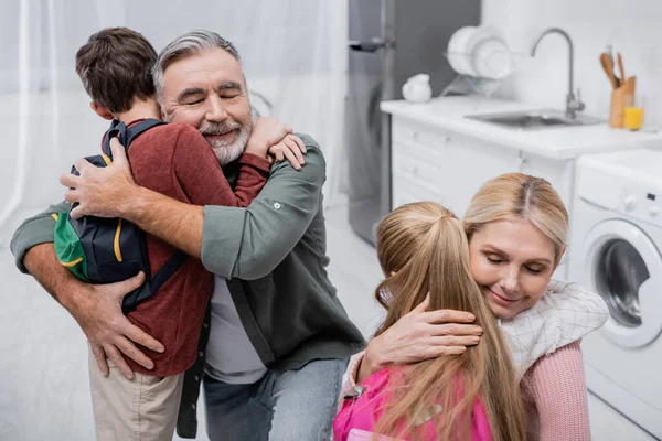 Heureux grands-parents embrassant petits-enfants avec sacs à dos à la maison — Photo de stock