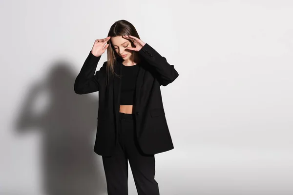 Brunetta in abito nero posa con le mani vicino al viso sul grigio con ombra — Foto stock