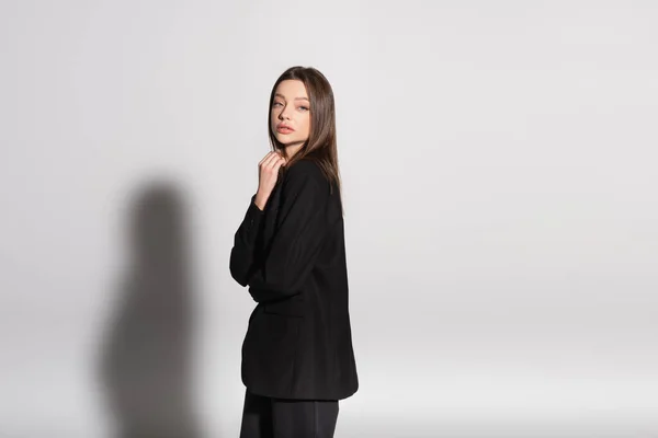 Young woman in black clothes looking at camera while standing on grey with shadow — Stock Photo