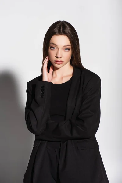 Hübsche junge Frau in schwarzen Kleidern blickt in die Kamera auf grau mit Schatten — Stockfoto