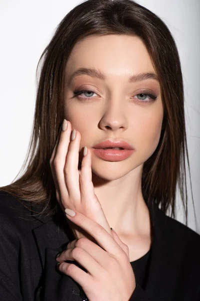 Close up view of young brunette woman touching face while looking at camera isolated on grey — Stock Photo