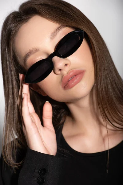 Крупним планом вид молодої брюнетки в чорних сонцезахисних окулярах ізольовані на сірому — стокове фото