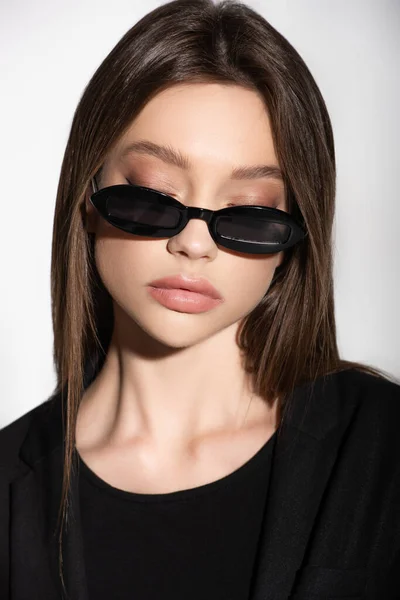 Portrait of young brunette woman posing in black sunglasses isolated on grey — Stock Photo