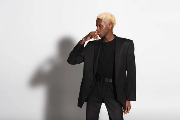 Uomo afro-americano alla moda che tocca le labbra guardando lontano sul grigio con ombra — Foto stock