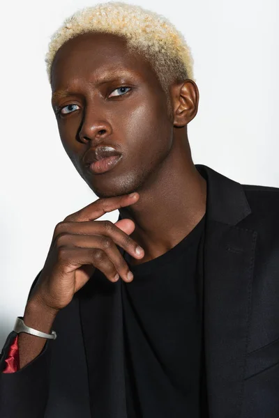 Élégant homme afro-américain avec les cheveux blanchis posant avec la main près du visage isolé sur gris — Photo de stock