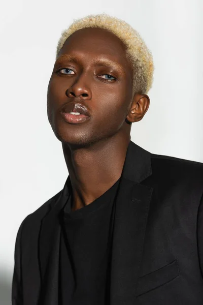 Porträt eines blonden afrikanisch-amerikanischen Mannes im schwarzen Blazer, der isoliert auf grau in die Kamera blickt — Stockfoto
