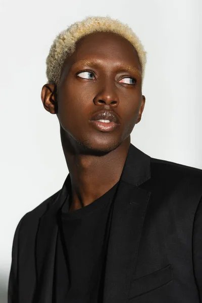 Retrato de un joven afroamericano con el pelo blanqueado mirando hacia otro lado aislado en gris - foto de stock