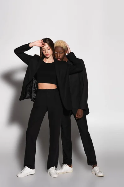 African american with bleached hair looking at camera near stylish woman on grey with shadow — Stock Photo