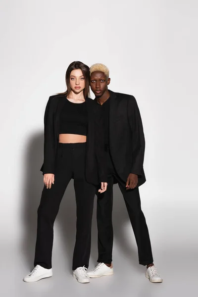 Full length view of blonde african american man and brunette woman looking at camera on grey with shadow — Stock Photo