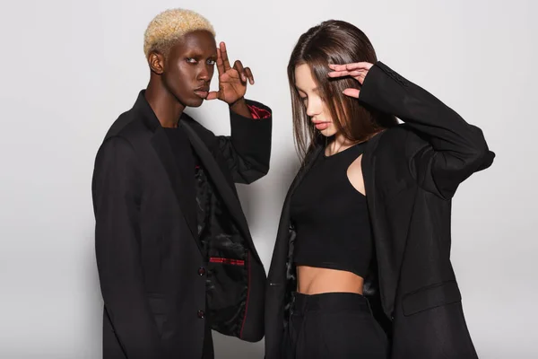 Young and stylish interracial couple in black clothes posing on grey — Stock Photo