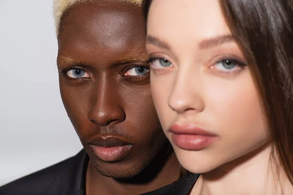 Vista de cerca de joven pareja interracial mirando a la cámara aislada en gris - foto de stock