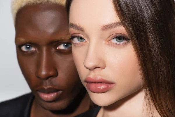 Close up view of brunette woman looking at camera near blurred african american man isolated on grey — Stock Photo