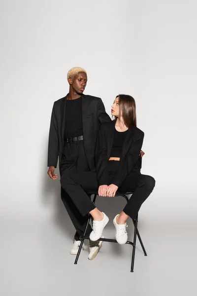 Trendy african american man and woman on chair looking at each other on grey with shadow — Stock Photo