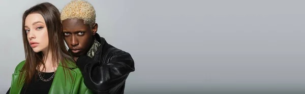 Афроамериканський чоловік з вибіленим волоссям, що спирається на плече брюнетки жінки ізольовані на сірому, банер — стокове фото