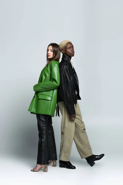 Brunette woman and blonde african american man in trendy clothes standing back to back on grey — Stock Photo