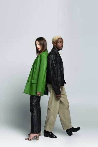 Vue pleine longueur de blond afro-américain homme et brune femme debout dos à dos sur gris — Photo de stock