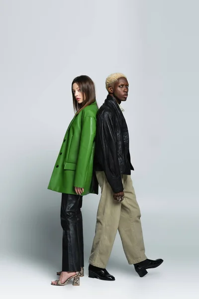 Full length view of blonde african american man and brunette woman standing back to back on grey — Stock Photo