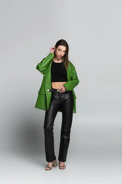 Vue pleine longueur de la femme tendance en pantalon en cuir noir sur gris — Photo de stock