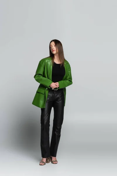 Ganzkörperansicht der Frau in grüner Jacke und schwarzer Lederhose auf grau — Stockfoto
