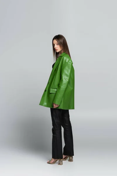 Ganzkörperansicht einer Frau in grüner Jacke, Lederhose und Sandalen auf grau — Stockfoto