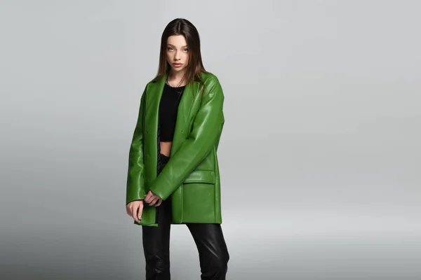 Young brunette woman in green leather jacket looking at camera isolated on grey — Stock Photo