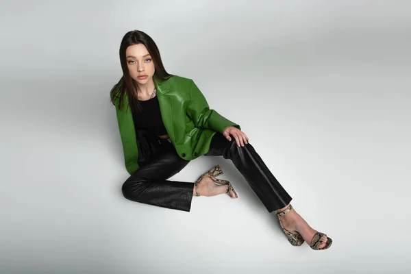 Frau in schwarzer Hose, grüner Jacke und Sandalen auf grau sitzend — Stockfoto