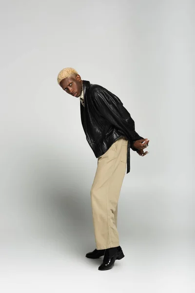 Glamour afro-americano homem com cabelos branqueados posando com as mãos atrás das costas em cinza — Fotografia de Stock