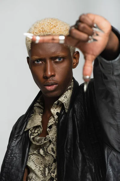 Glamour african american man posing with metal fingernails on blurred hand isolated on grey — Stock Photo